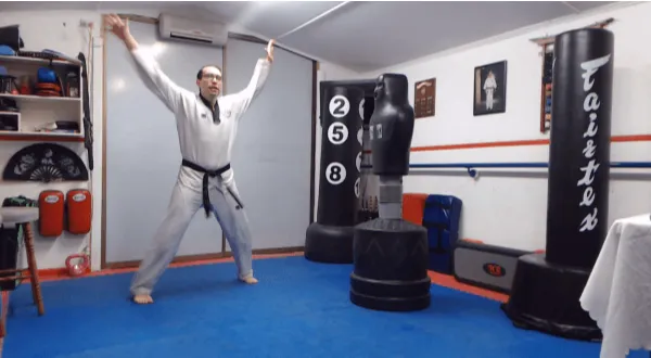 Martial arts instructor doing jumping jacks in a dojo training room.