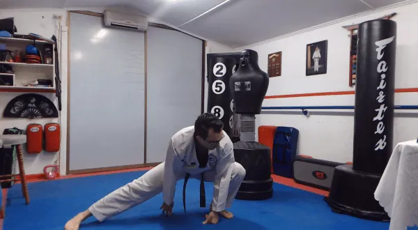 Martial arts instructor doing a side lunge stretch in a dojo.