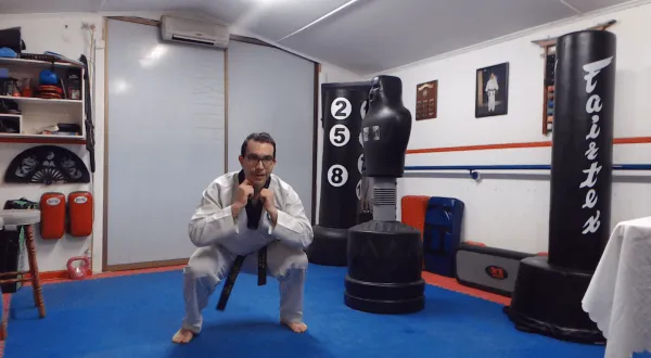 Martial arts instructor performing a squat exercise in a dojo.