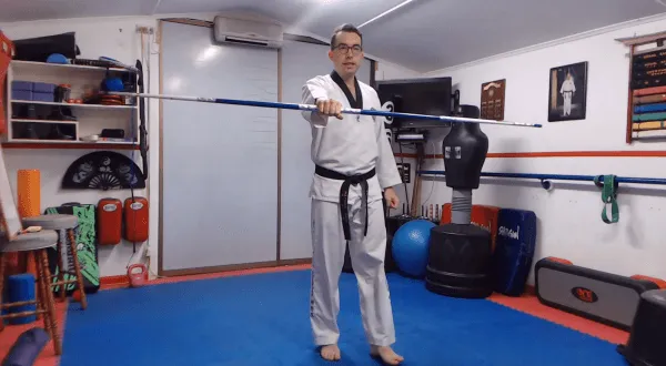 Martial arts instructor demonstrating a bo staff technique in a dojo.