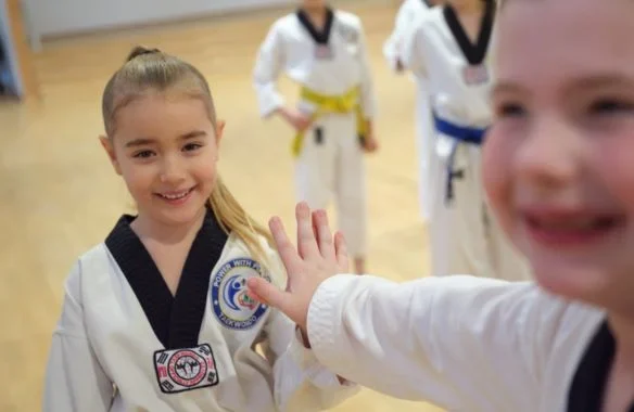 Young Taekwondo students smiling and interacting during a martial arts class.
