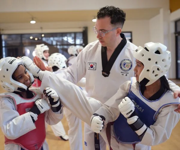 Taekwondo instructor coaching two students wearing protective gear during a sparring practice.