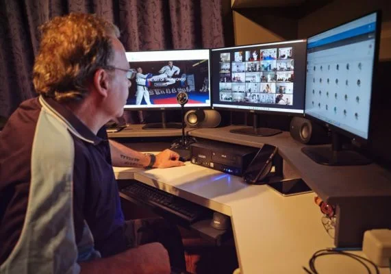 Instructor managing an online Taekwondo class using multiple computer screens during a virtual training session.