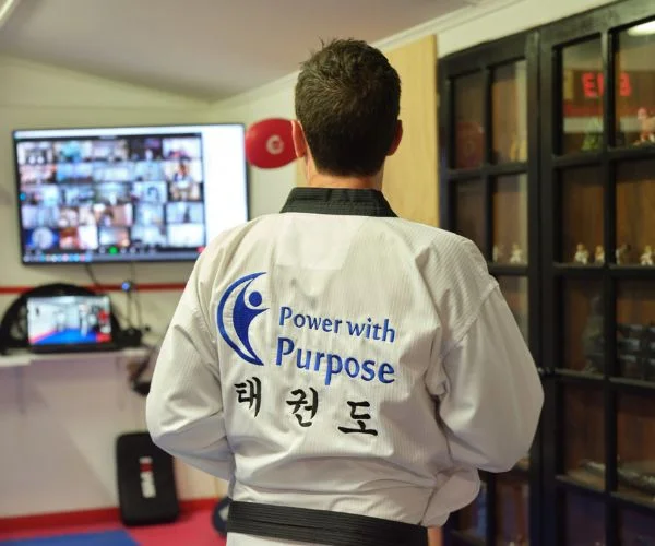 Taekwondo instructor wearing a “Power with Purpose” uniform participating in an online martial arts class.