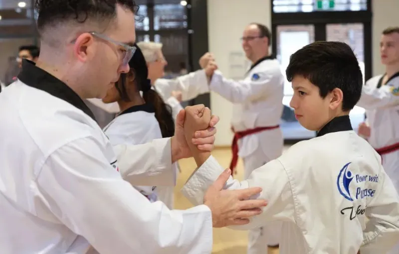 Martial arts instructor guiding a young student through technique during a training session in a class setting