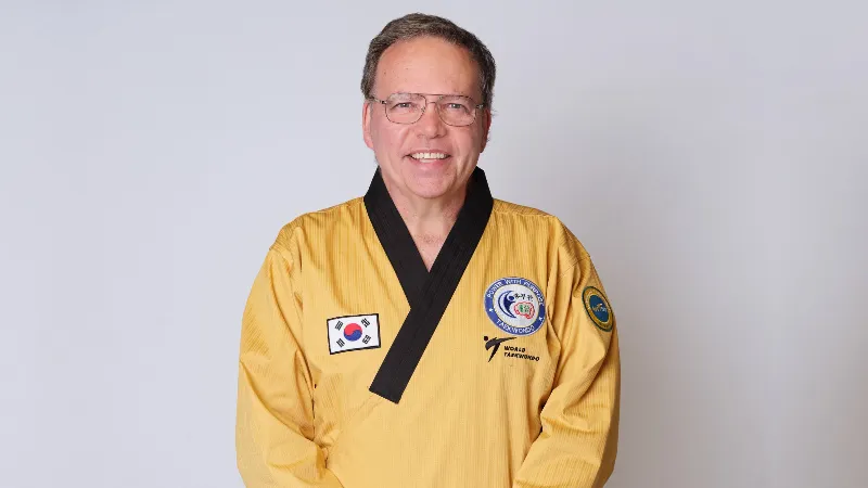 Taekwondo instructor wearing a yellow uniform standing against a plain background.