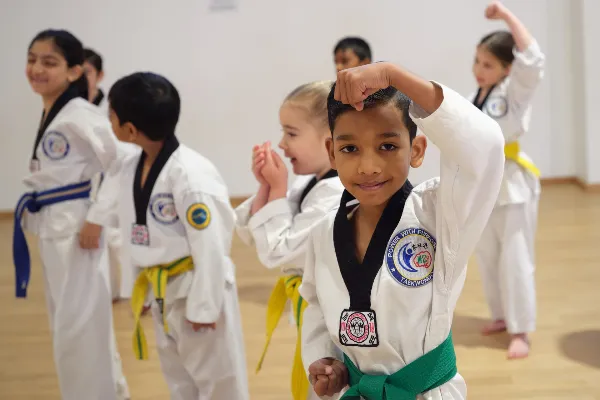 Children in taekwondo uniforms with coloured belts practising punches during a martial arts training class.