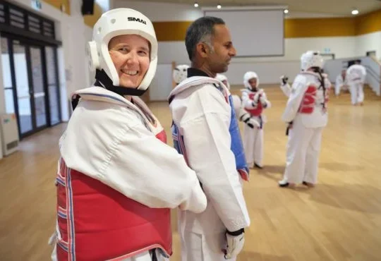 Taekwondo students wearing protective gear preparing for sparring during a martial arts class.
