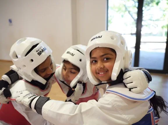 Young Taekwondo students wearing protective gear hugging together during sparring practice.