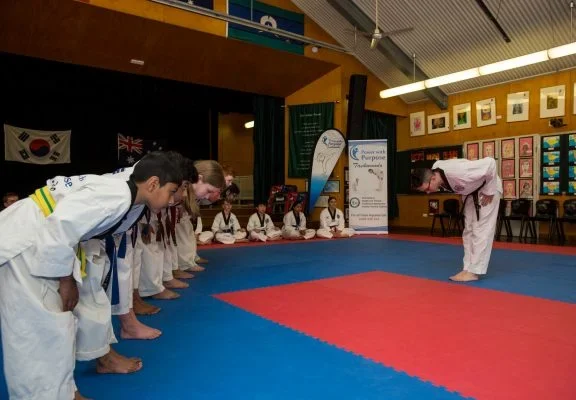 Taekwondo students bowing to an instructor on a training mat before beginning practice.